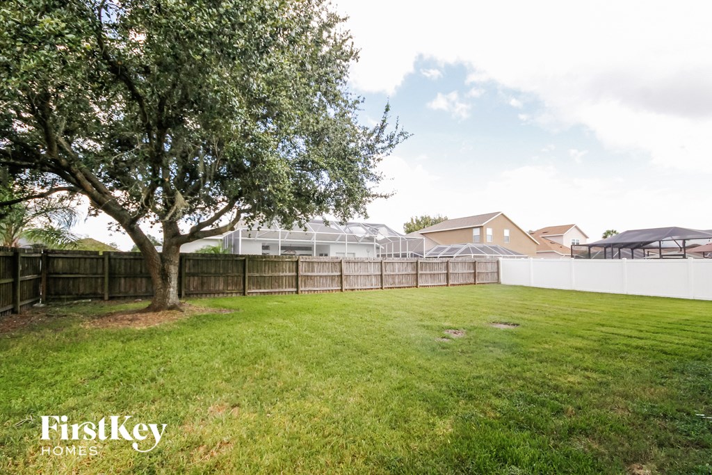 A tree in a grassy area with a fence and houses in the background.