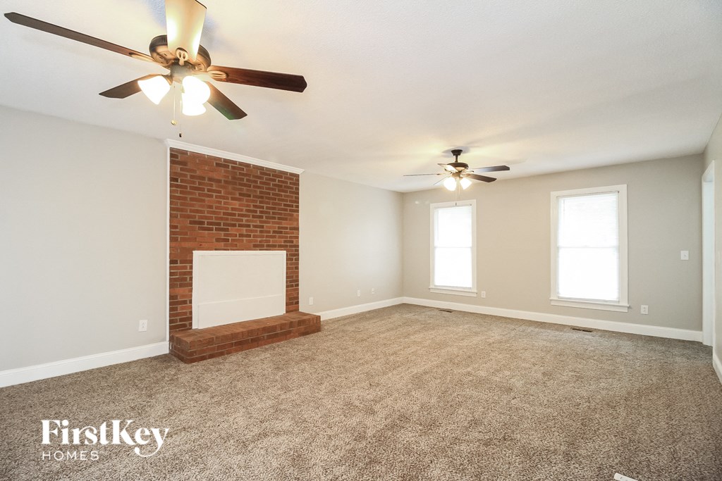 an empty living room with a brick fireplace and two ceiling fans