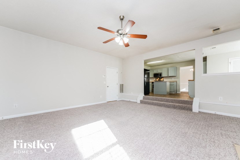 an empty living room with a ceiling fan and a kitchen