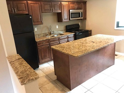 A kitchen with a black refrigerator and brown cabinets.