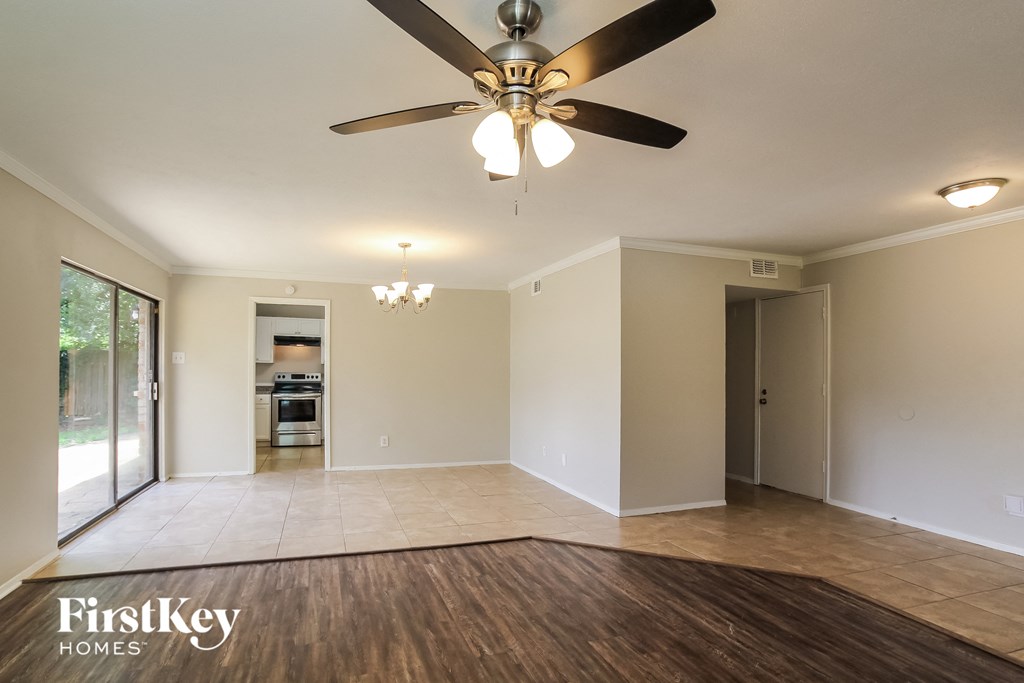 an empty living room with a ceiling fan and a door to the kitchen