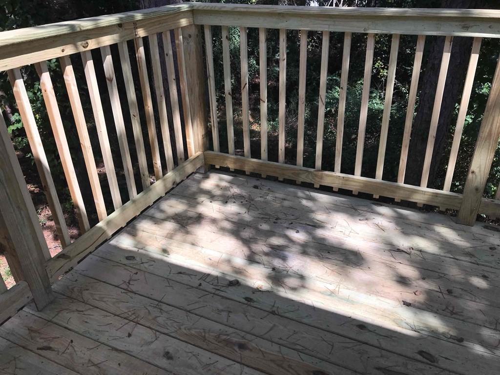 A wooden deck with a railing and shadow of the railing on the floor.