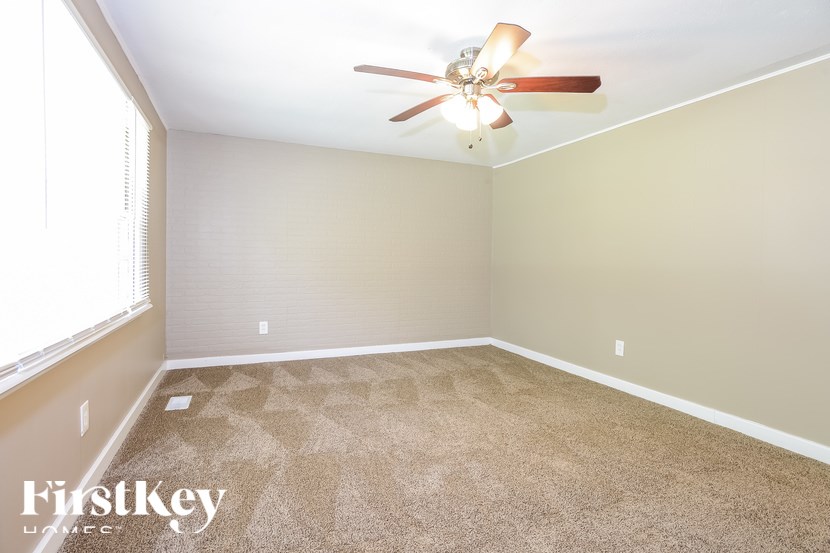 A carpeted room with a ceiling fan and a window.