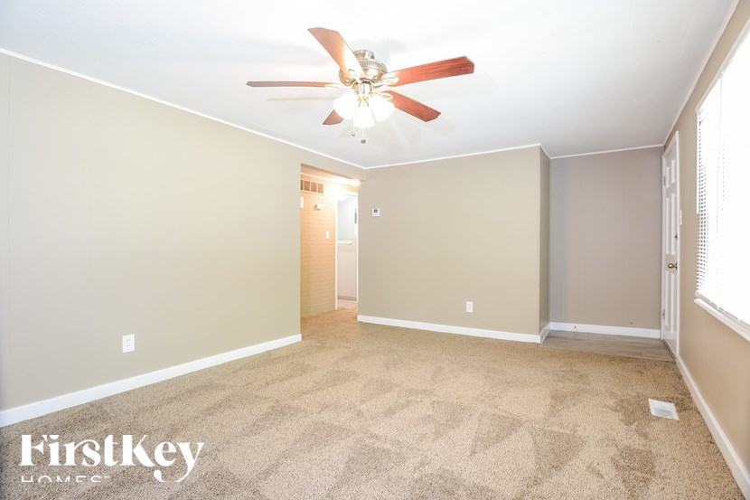 A carpeted room with a ceiling fan and a door in the background.