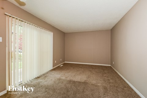 a carpeted living room with a large window and white curtains