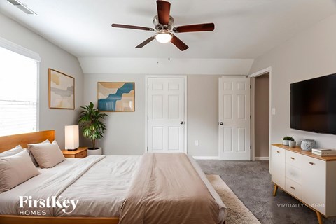 A bedroom with a bed, a ceiling fan, and a painting on the wall.