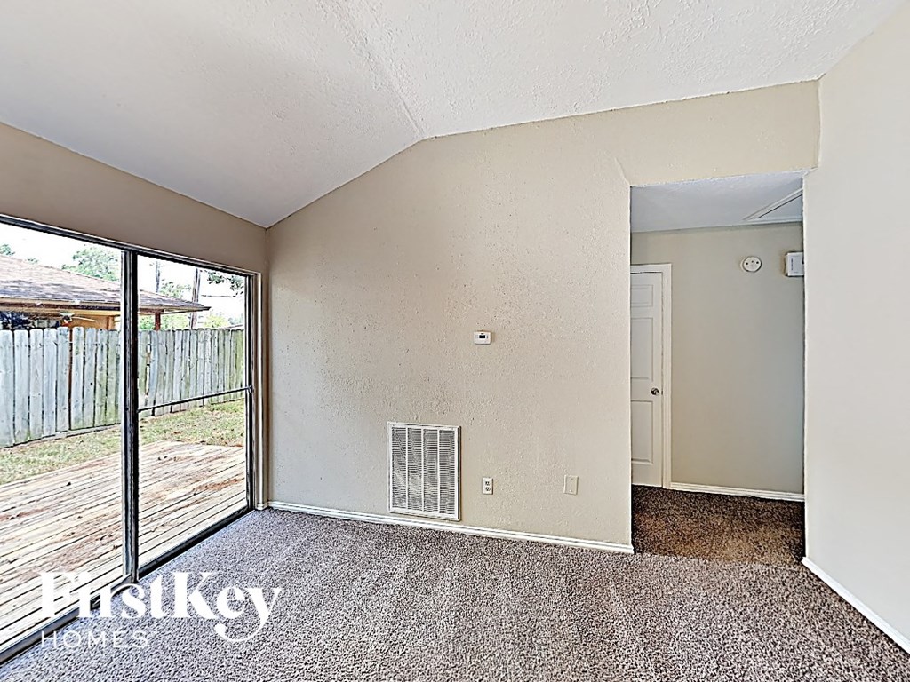 A room with a carpeted floor and a sliding glass door leading to a backyard.