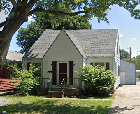 A small white house with a red door and a porch.