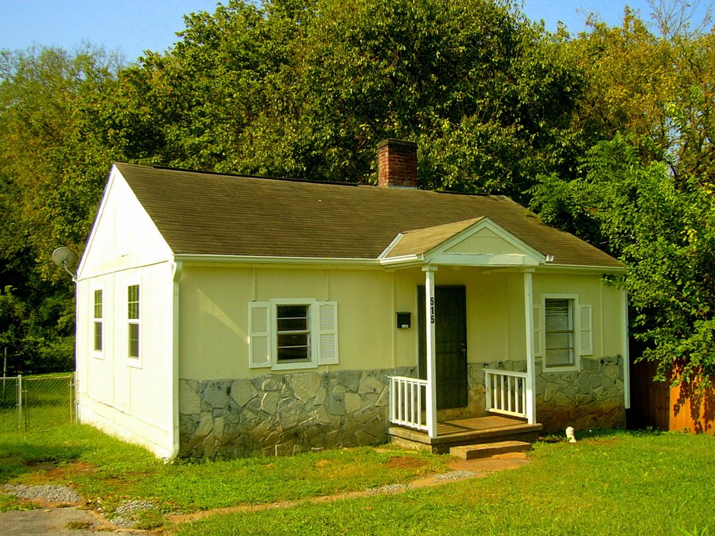 a small white house with a porch in front of trees