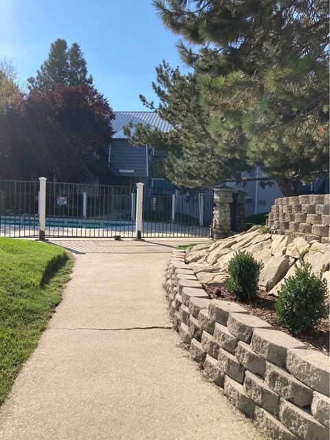 A concrete walkway leads to a metal fence and a building.