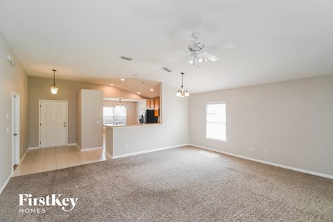 an empty living room with a ceiling fan and a kitchen