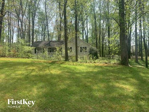 A house is surrounded by trees in a grassy area.