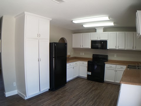 A black refrigerator and oven in a kitchen with white cabinets.