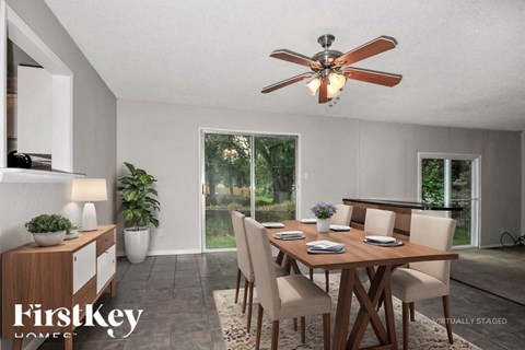 A dining room with a wooden table and chairs, a ceiling fan, and a potted plant.