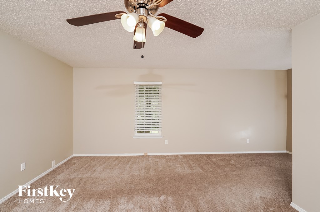 the spacious living room with ceiling fan and carpeting