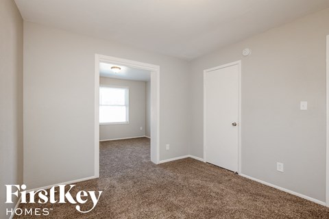 a bedroom with white walls and carpet and a door to a closet