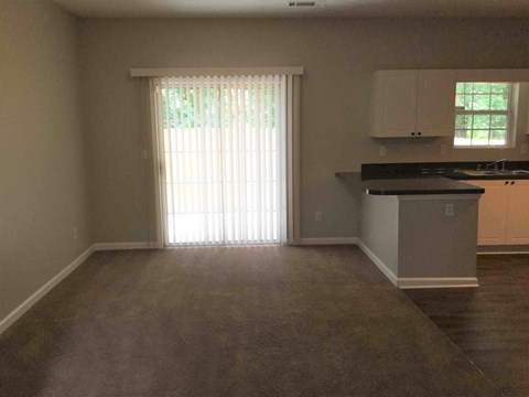 an empty living room with a door to a kitchen