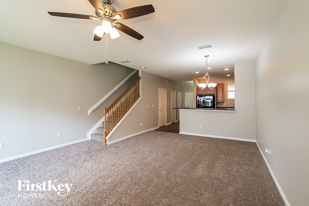 A spacious living room with a carpeted floor and a staircase leading to the upper level.