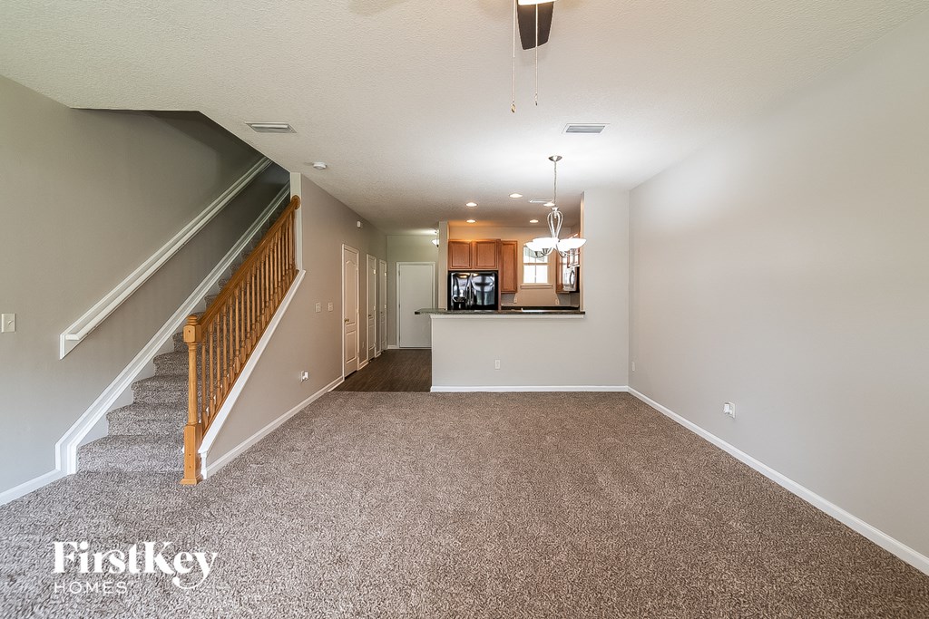 A spacious living room with a staircase on the left side and a dining area in the background.