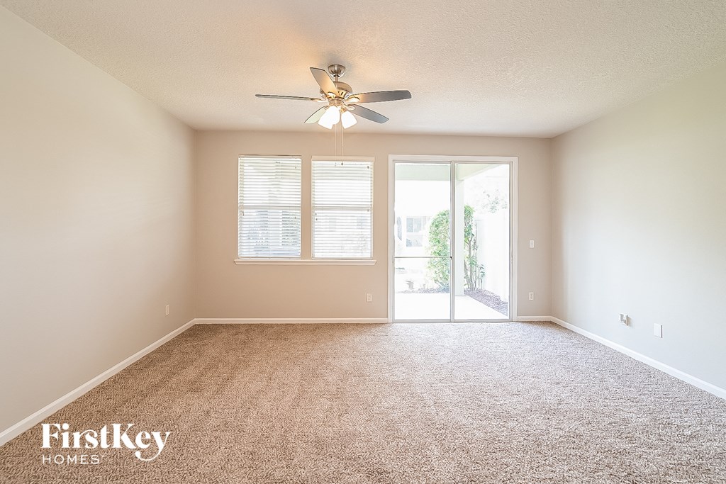 A spacious room with a carpeted floor, a ceiling fan, and sliding glass doors.