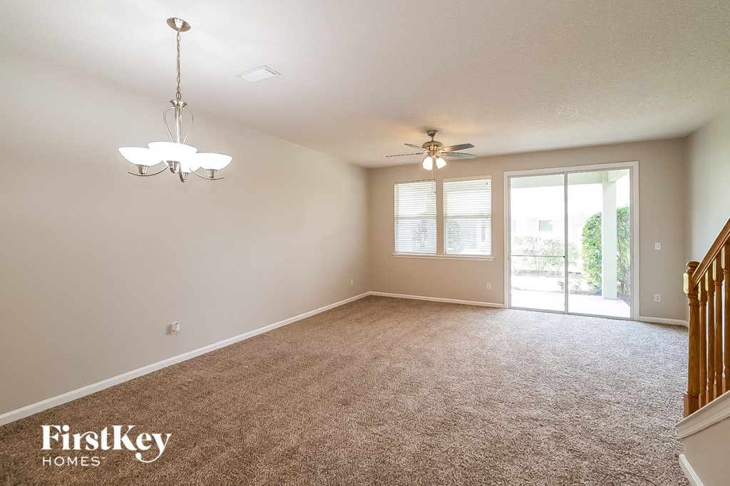 A spacious room with a carpeted floor, a chandelier, and a ceiling fan.