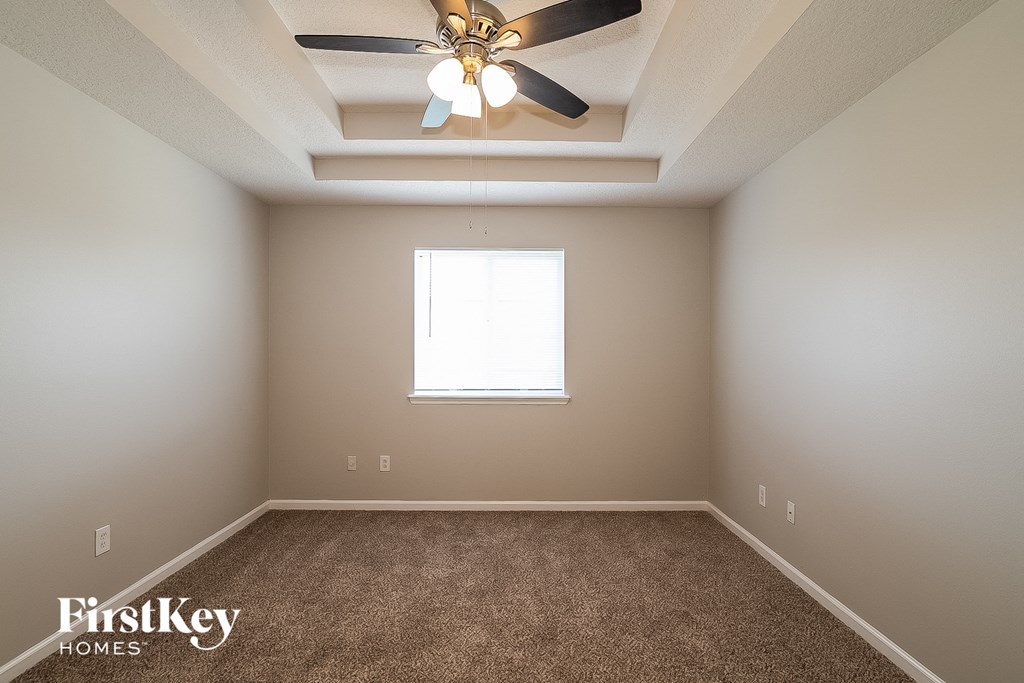 A room with a carpeted floor, a ceiling fan, and a window.