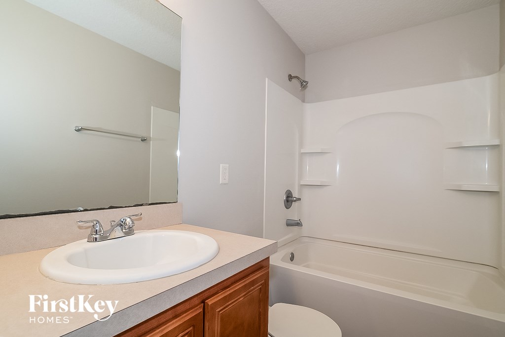 A white bathroom with a sink, mirror, and bathtub.