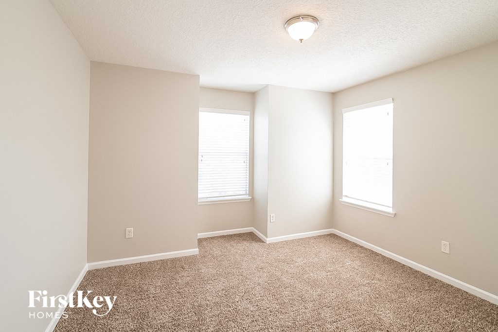 A room with a carpet floor and two windows.