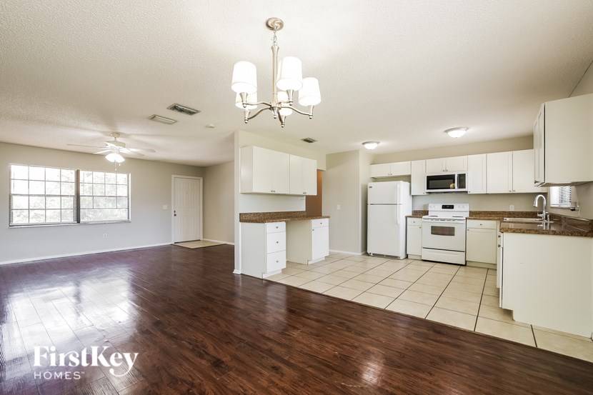 A well-lit, spacious kitchen and living room with wooden floors and white appliances.