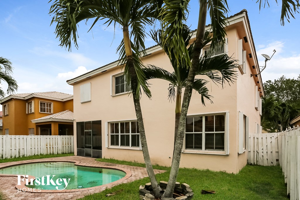 A palm tree stands in front of a house with a pool.