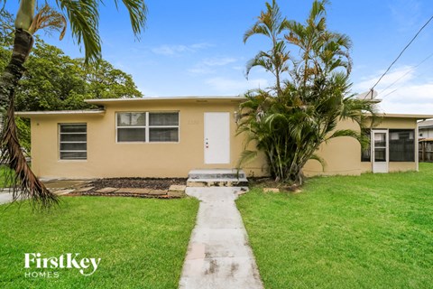 a small yellow house with a lawn and palm trees
