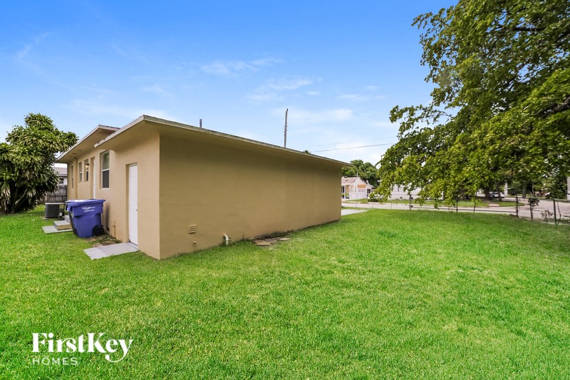 a small beige house with a yard and a blue trash can
