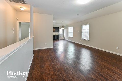 an empty living room with wood flooring and a kitchen