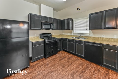 a kitchen with black cabinets and black appliances and a wooden floor