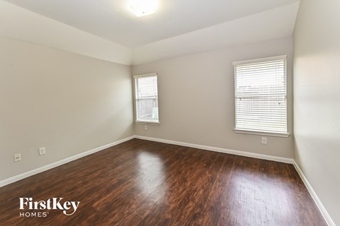 a living room with wood flooring and white walls and two windows