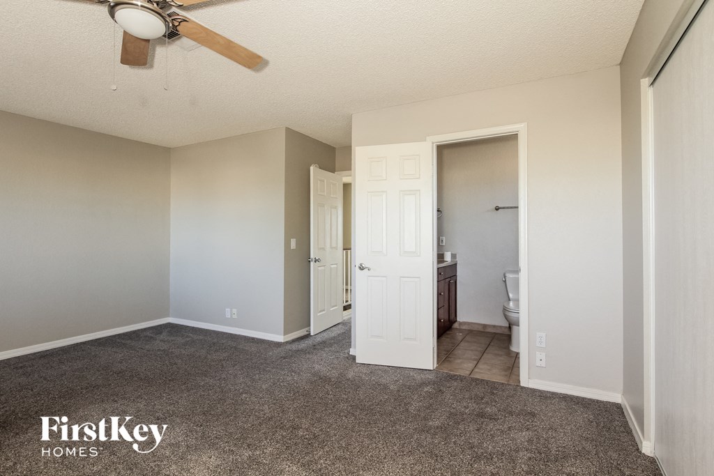an empty living room with a ceiling fan and a door to a bathroom