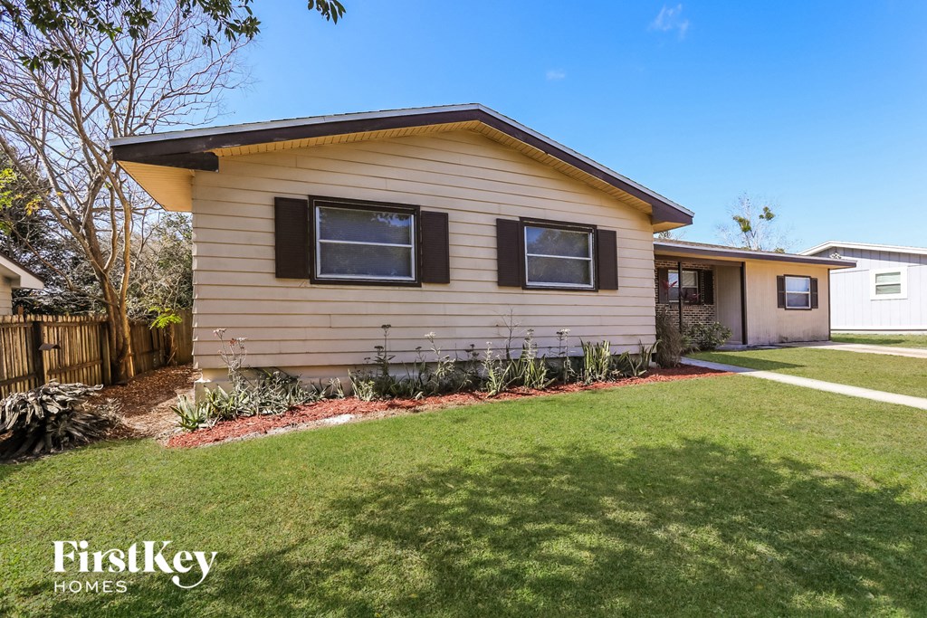 A beige house with a brown roof and a white fence.