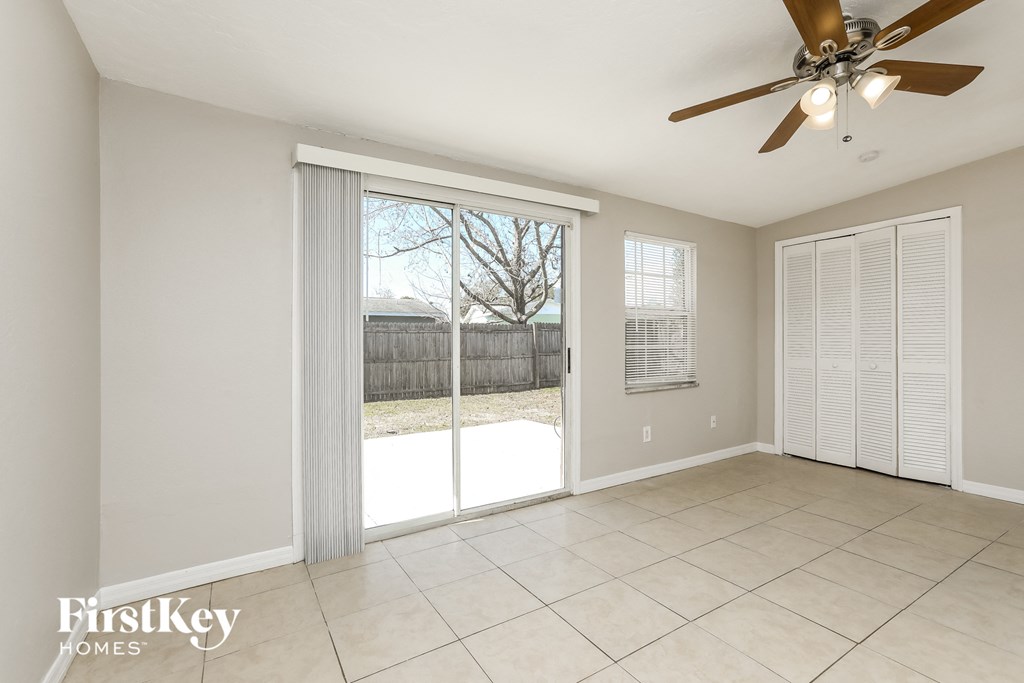 A spacious room with a ceiling fan and sliding glass doors leading to a backyard.
