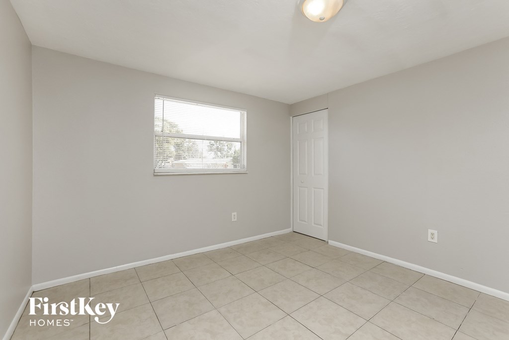 A room with a white door and a window with a view of trees.