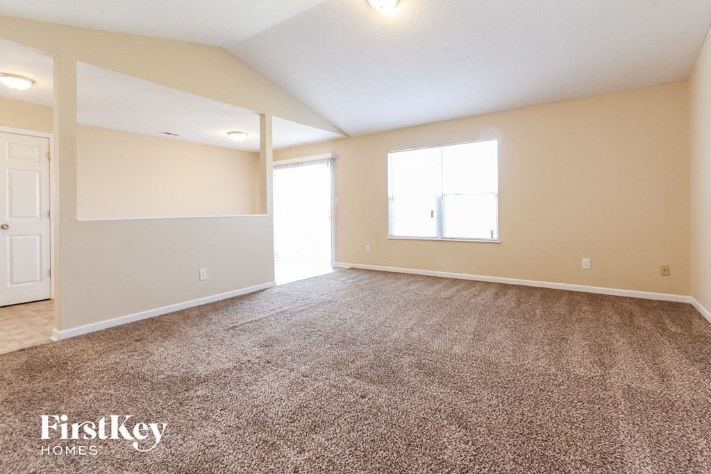 A spacious room with a carpeted floor and a door on the left side.