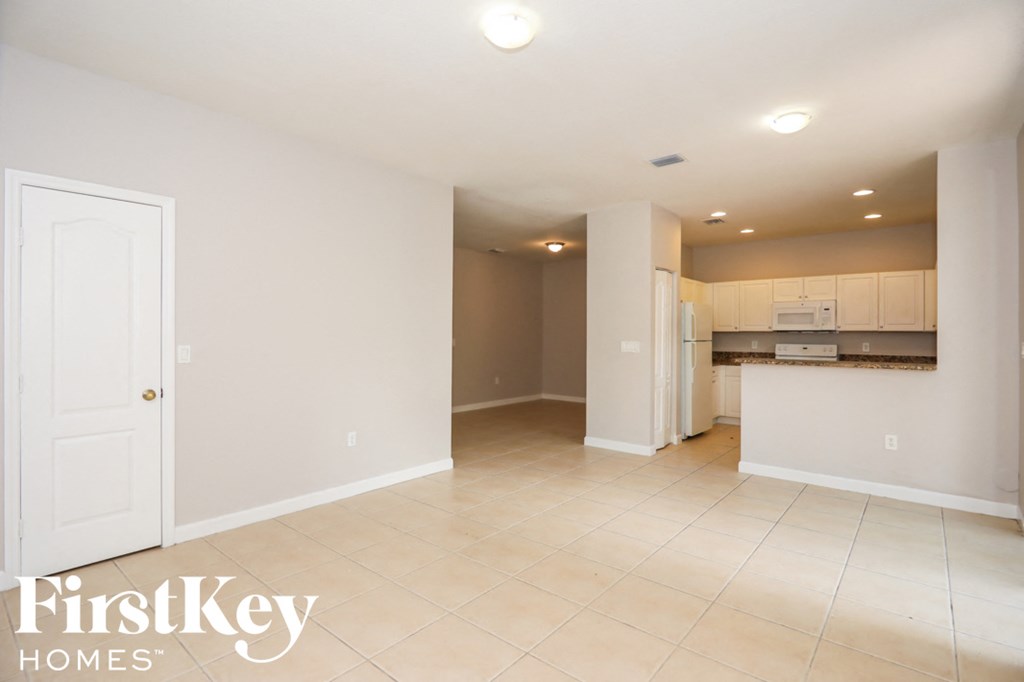 an empty living room and kitchen with white cabinets and tiled floors