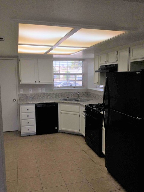 A black refrigerator sits in a kitchen with white cabinets and a black dishwasher.