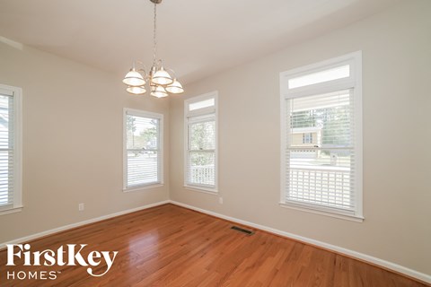 an empty dining room with a wood floor and three windows