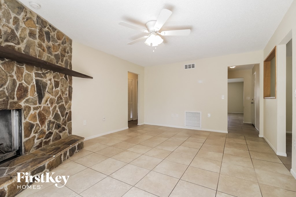 an empty living room with a stone fireplace and tile flooring
