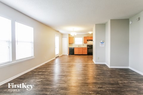 A spacious room with wooden flooring and a kitchen area in the background.