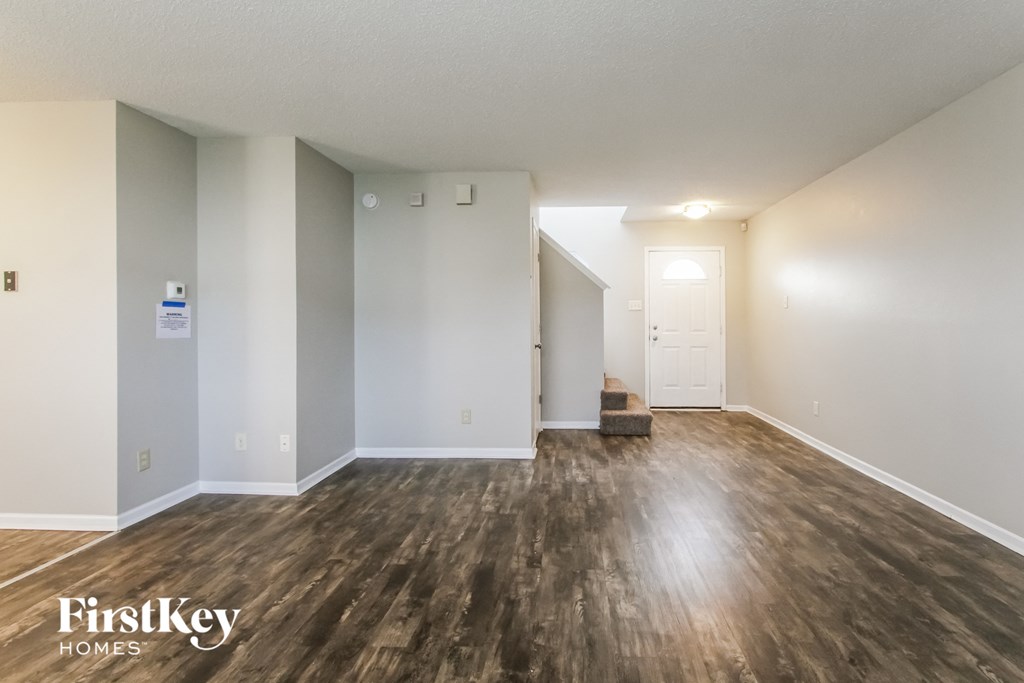 A room with wooden flooring and white walls, with a door on the right side.
