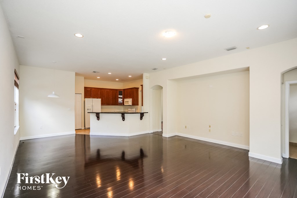 an empty living room and kitchen with wood floors and white walls