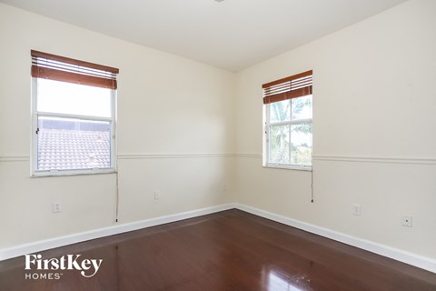 a bedroom with white walls and wood floors and two windows