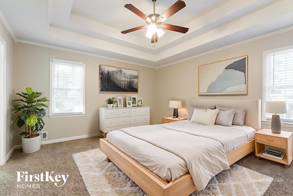 A bedroom with a large bed, a ceiling fan, and a painting on the wall.