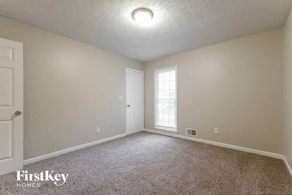 A room with a carpeted floor, a door, and a window with blinds.